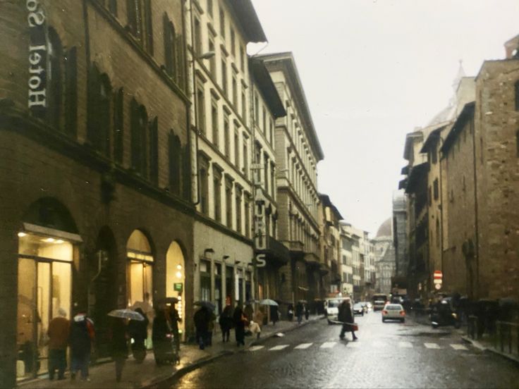 people are walking down the street with umbrellas in front of buildings on a rainy day