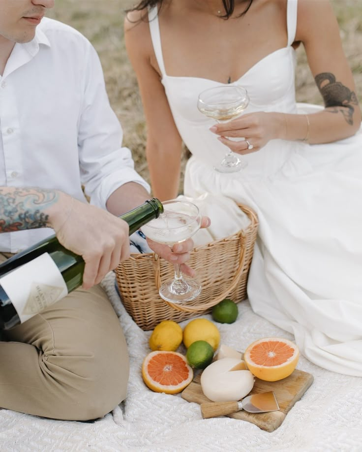 a man and woman sitting next to each other holding wine glasses in front of oranges