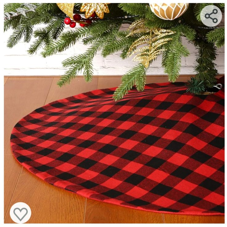 a red and black plaid christmas tree skirt on top of a wooden floor next to a potted plant