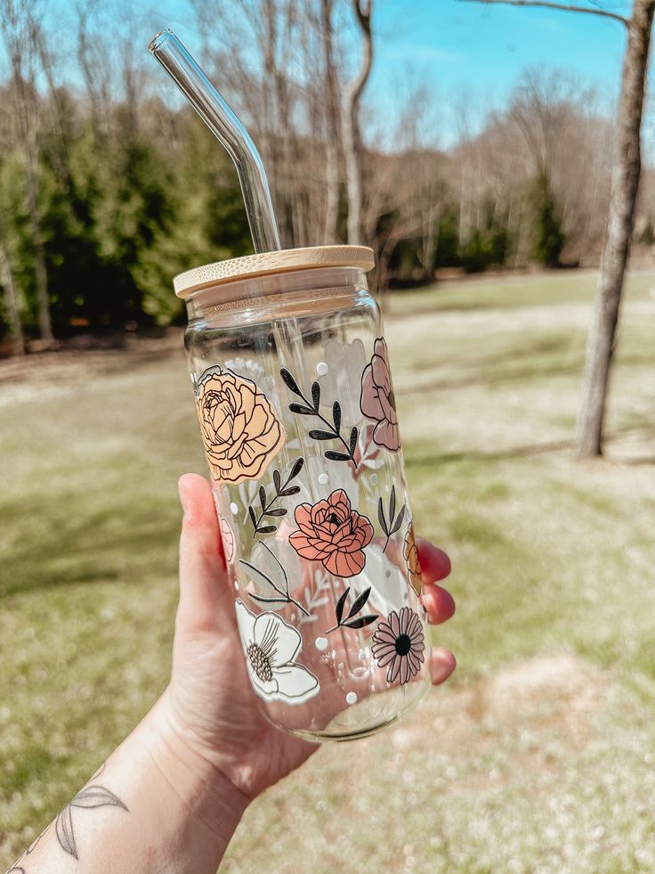 a hand holding a glass with a straw in it and flowers painted on the side