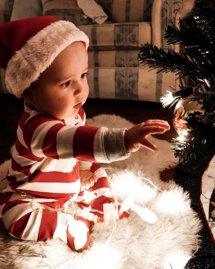 a baby wearing a santa hat sitting next to a christmas tree