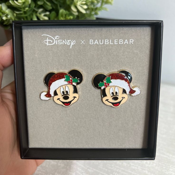 a pair of mickey mouse christmas themed earrings in a box with a plant behind it