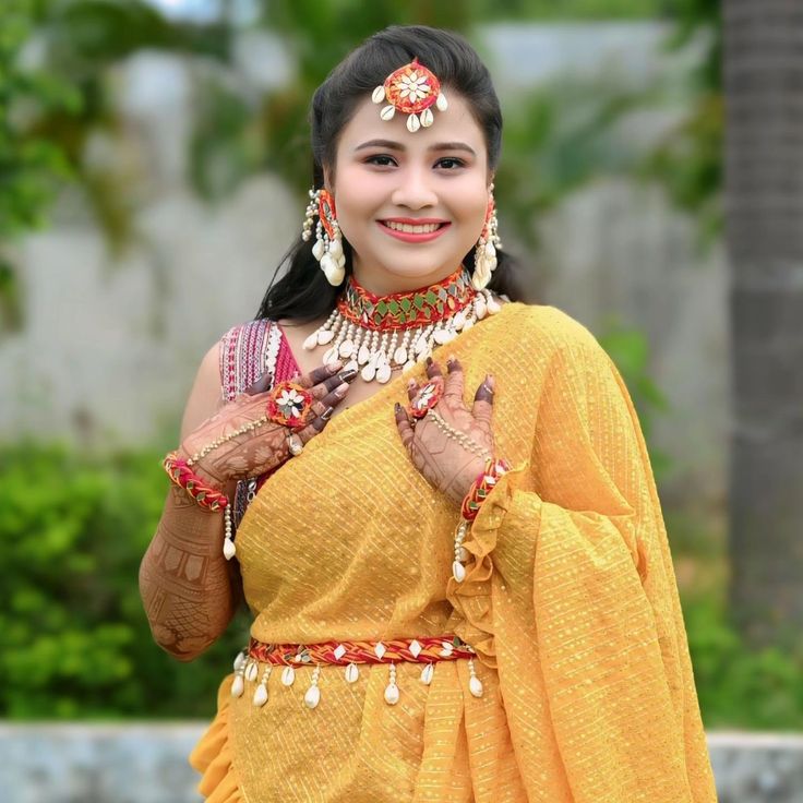 a woman in an orange sari with jewelry on her head and hands, smiling at the camera