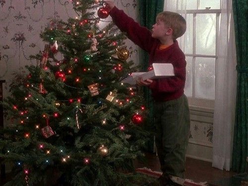 a young boy decorating a christmas tree in his living room with the lights on