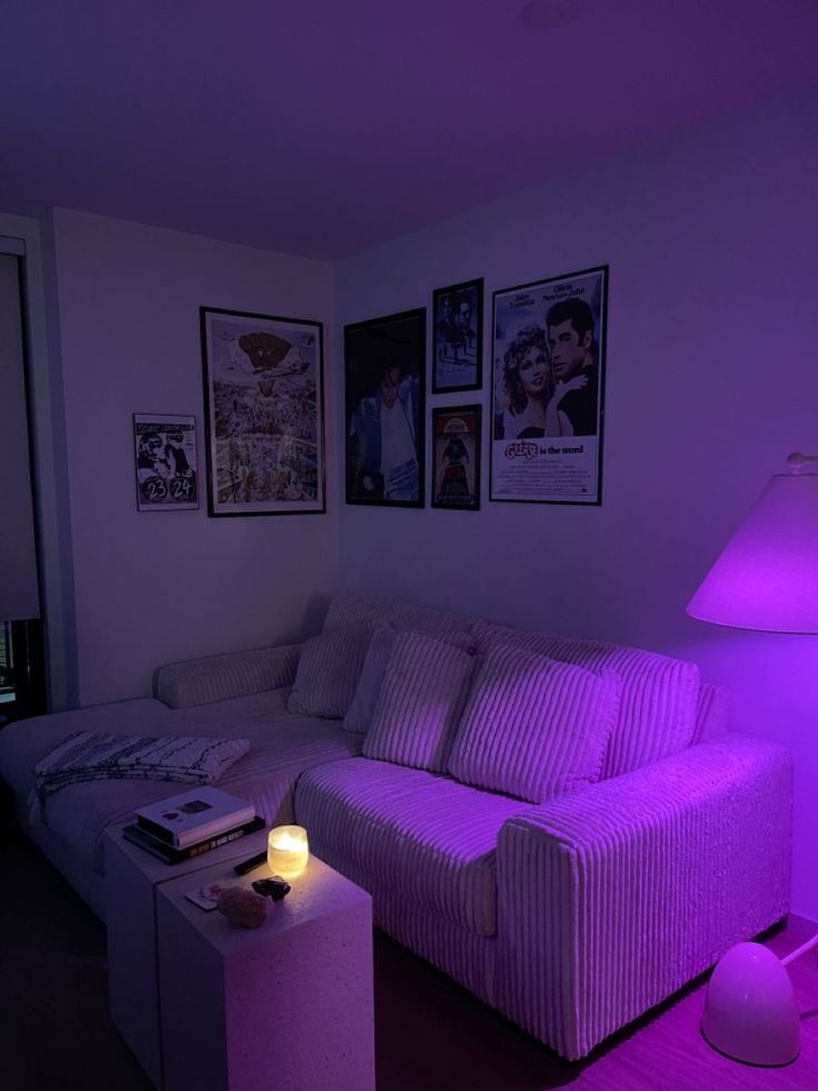 a living room with purple lighting and pictures on the wall above the white couches