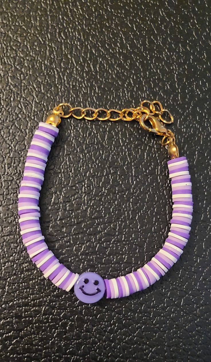 a purple and white bracelet with a smiley face beaded on the end, hanging from a gold chain