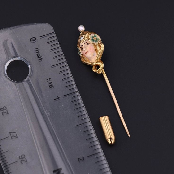 During the turn of the nineteenth century, artisans were inspired by the changing roles of women in society and began depicting the free flowing feminine form in brooches, bracelets, rings and more. This antique stickpin (circa 1890-1900) features a woman of 14k gold, adorned in enamel with a single diamond crown and a pearl accent. The pin head measures 0.9 inches by 0.5 inches wide with the entire pin measuring 1.9 inches long. It is in very good condition; however there is a chip to the ename Yellow Gold Enamel Brooches, Victorian Style Enamel Pin Gift, Victorian Brooches For Ceremonial Occasions, Gold Formal Enamel Pin, Art Nouveau Brooch For Formal Occasions, Art Nouveau Yellow Gold Collectible Brooches, Art Nouveau Formal Jewelry Brooch, Art Nouveau Enamel Brooch Jewelry, Victorian Enamel Brooches For Formal Wear