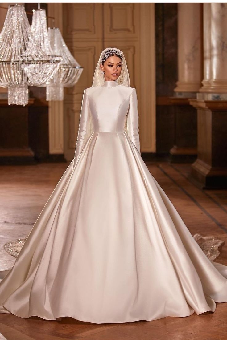 a woman in a white wedding dress standing on a floor with chandelier behind her