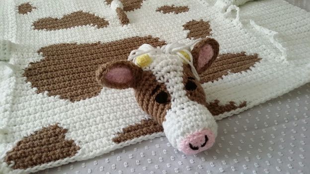 a brown and white cow laying on top of a bed next to a crocheted blanket