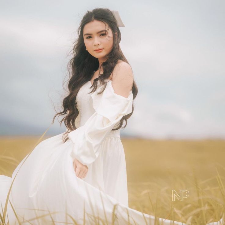 a woman in a white dress is standing in the middle of a field with tall grass