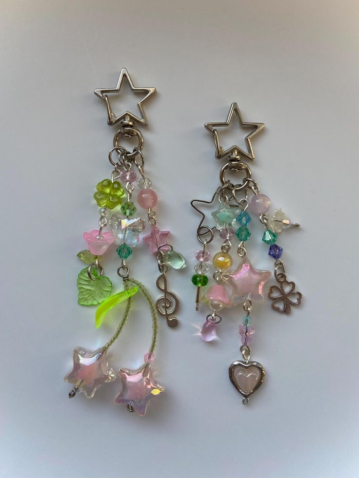 two pairs of earrings with charms attached to them on a white surface, one has a heart and the other has a star