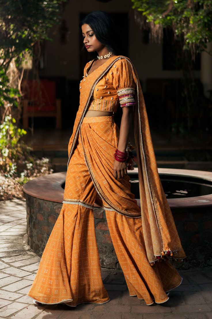 Mustard bandhej print pre-draped sharara pant saree. Comes along with a padded blouse with crystal shell ornamentation.
Components: 2
Pattern: Print
Type Of Work: Bandhej
Neckline: Square Neck
Sleeve Type: Puff Sleeves
Fabric: Silk, Georgette
Color: Yellow
Other Details: 
Blouse:
Padded
Cutdana, gota and sequin embroidered cuffs
Saree:
Gota patti detail border
Occasion: Sangeet - Aza Fashions Pant Saree, Bandhej Print, Saree Gowns, Dhoti Saree, Cotton Sarees Handloom, Embroidered Cuffs, Sharara Pants, Drape Pants, Character Clothing