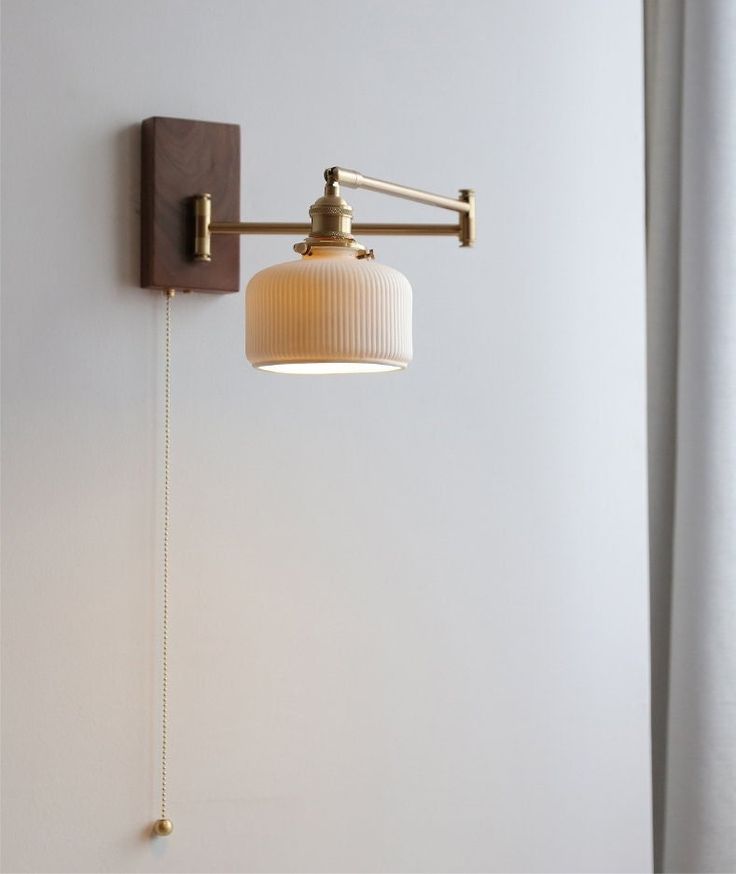 a wall light with a white shade hanging from it's side