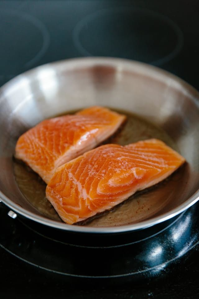 two raw salmon fillets in a pan on the stove