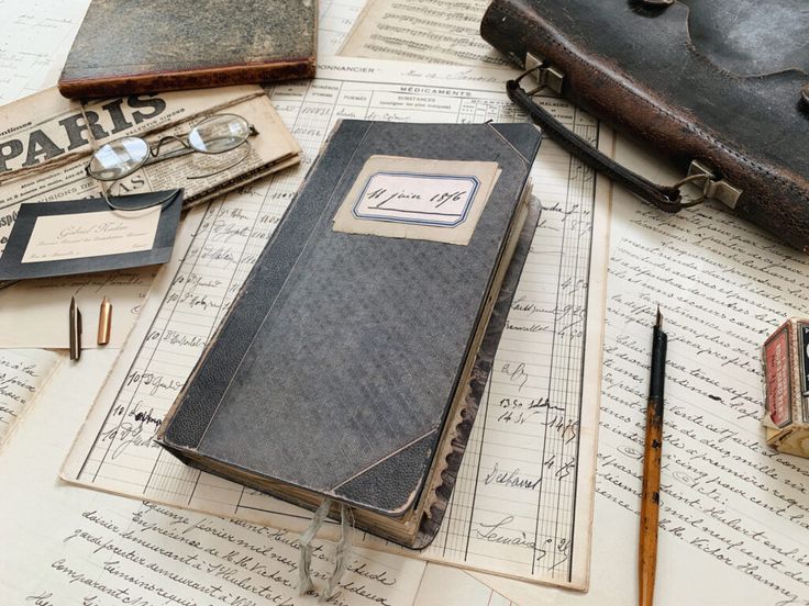 an old book sitting on top of papers with writing and other items around it,