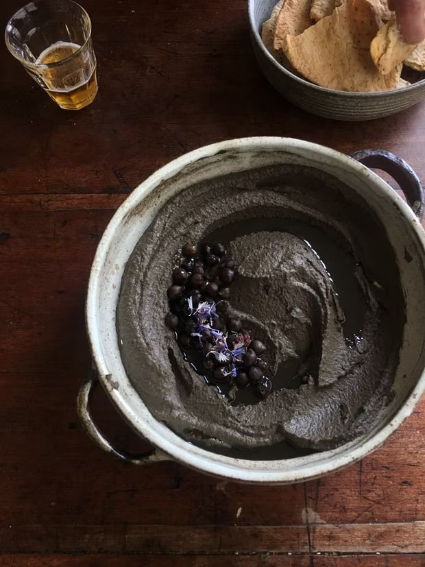 a bowl filled with black beans and chips next to a glass of beer on a wooden table