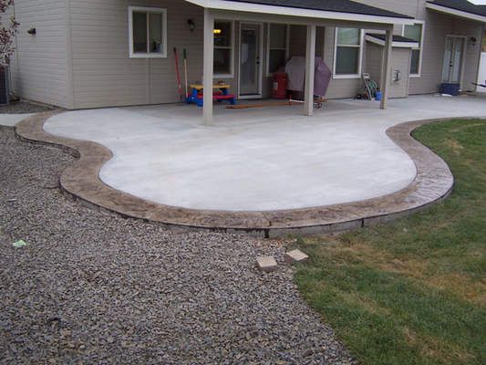 a house with a patio and covered in concrete next to a yard area that has gravel on the ground