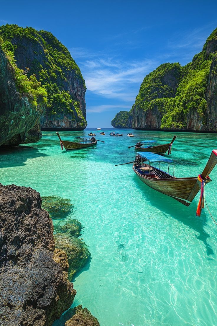 three boats are anchored in the clear blue water near rocky cliffs and green trees on either side