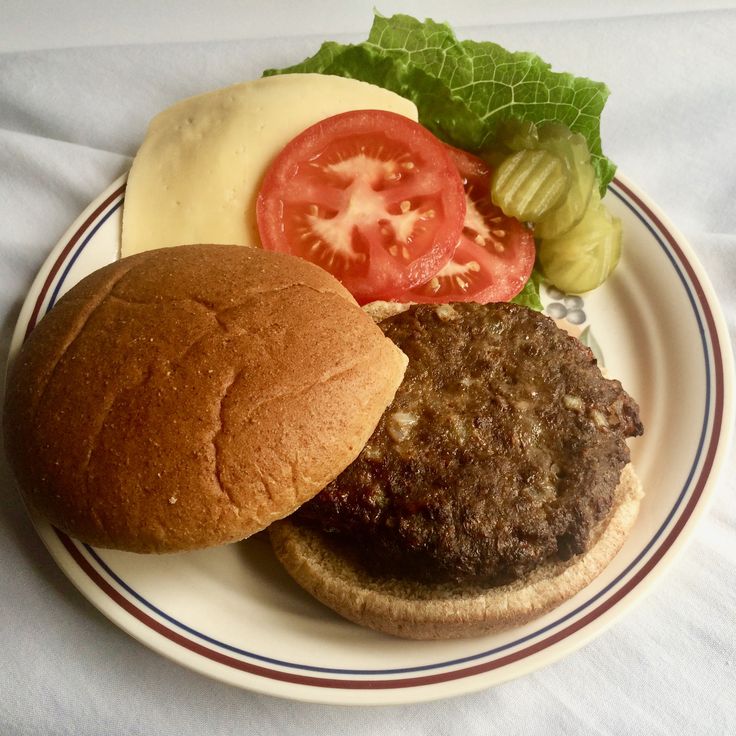 a hamburger with lettuce, tomato and cheese is on a plate next to a pickle