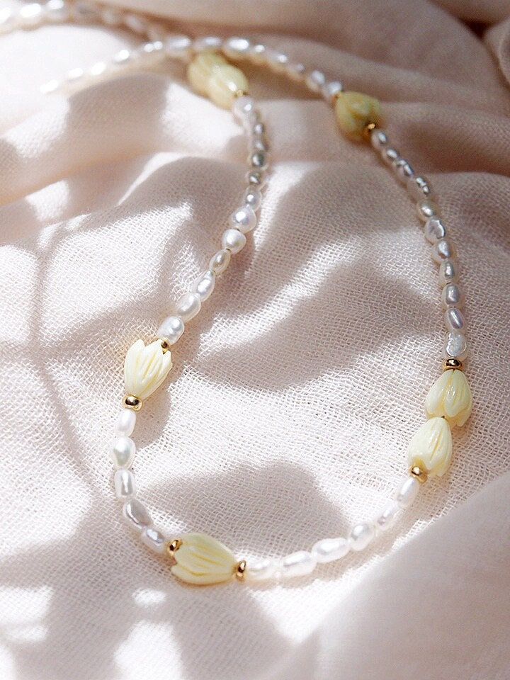 "Inspired by traditional Hawaiian leis gifted as tokens of hospitality, this handmade gold and pearl necklace features a glistening collection of pearls, gold beads and pikake flower blossoms. ✦ DETAILS ✦ ✧ Name: Mele (MEH-leh) - Song. ✧ Adjustable Length from: 16\"-18\". ✧ White Freshwater Pearls. ✧ Carved Resin Pikake Beads ✧ 14kt Gold Filled Components, Extender, and Clasp. ✧ All Ke Aloha Jewelry pieces come packaged thoughtfully, beautifully, and ready for gift giving. ✦ MORE GOLD NECKLACES Handmade Yellow Pearl Necklaces, Yellow Pearl Beaded Necklaces As Gift, Yellow Gold Beaded Pearl Necklace For Wedding, Wedding Yellow Gold Beaded Pearl Necklace, Handmade Yellow Pearl Necklace For Gift, Yellow Pearl Necklaces With Round Beads, Cream Pearl Pendant Necklace, Yellow Beaded Pearl Necklace, Delicate Beaded Necklace With Pearl Pendant As Gift