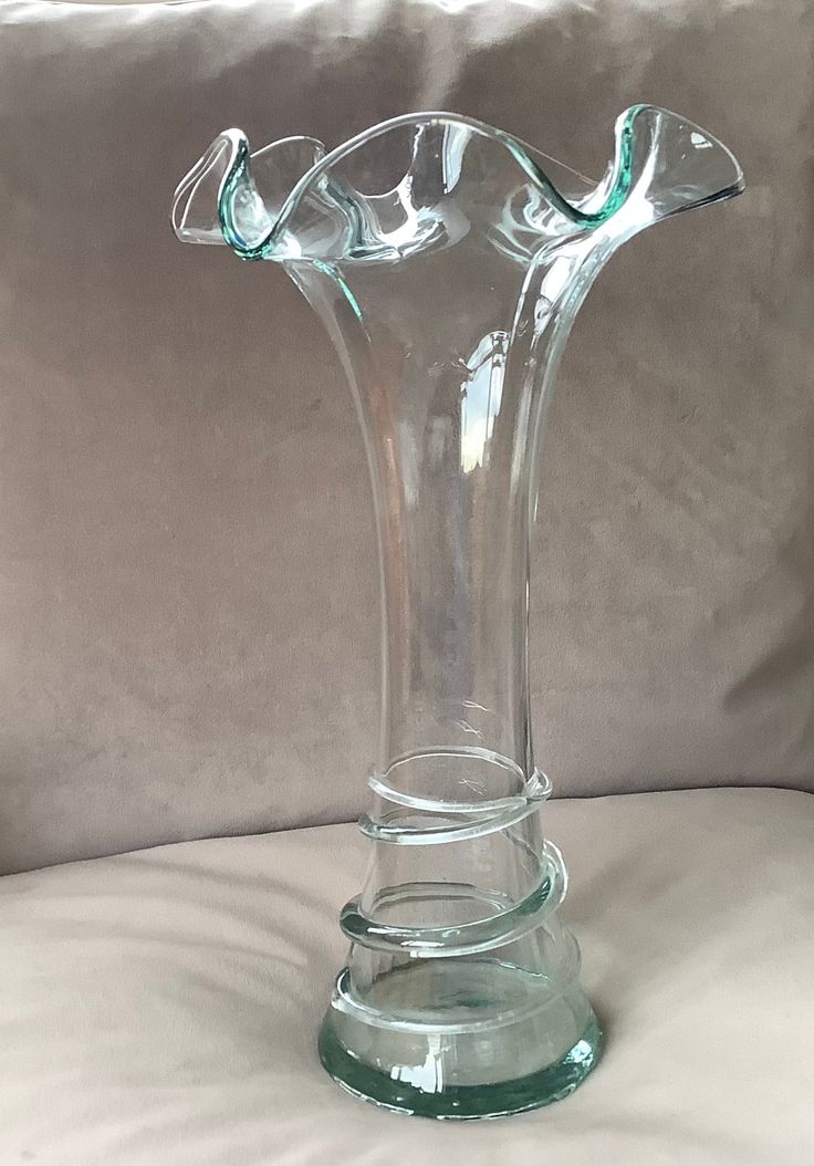 a clear glass vase sitting on top of a white bedding sheet with a pillow behind it