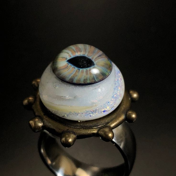 Hazel eye with swirls of rainbow Dichro amongst the white glass! The bezel is bronze, in the ring band is wide and made of Stainless steel! Of course I did the glass and had the bronze casted! Size Bronze bezel 1 inch wide 1/8 tall Eye 5/8 wide. 1/2 inch tall Ring band size 9 1/4 wide Eye Rings Jewelry, Handmade Mystical Iridescent Ring, Handmade Iridescent Mystical Ring, Mystical Handmade Iridescent Ring, Glass Eye Jewelry, Unique Eye-shaped Jewelry For Gifts, Eyeball Ring, Spiritual Eye-shaped Sterling Silver Jewelry, Eyes Ring