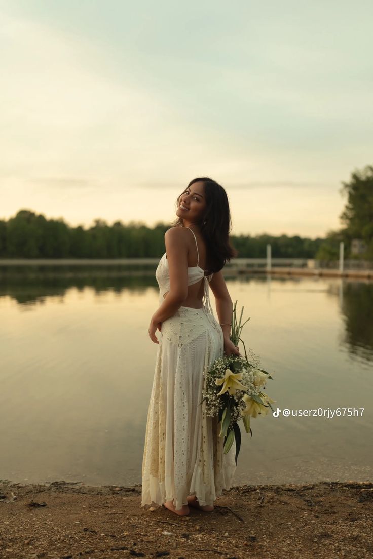 a woman in a white dress is standing by the water