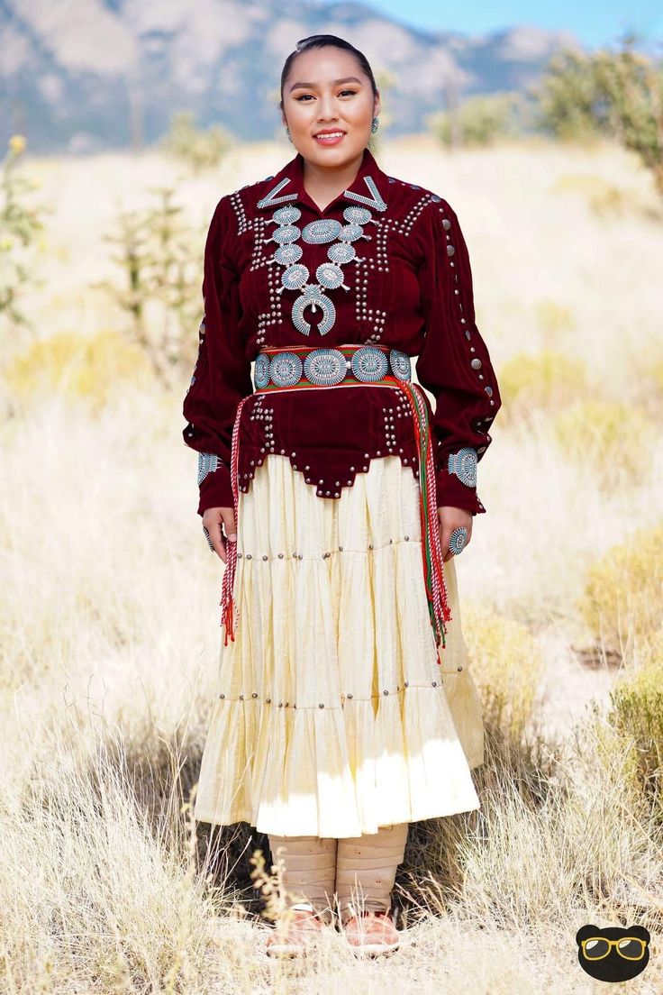 a woman standing in the middle of a field wearing a red shirt and white skirt