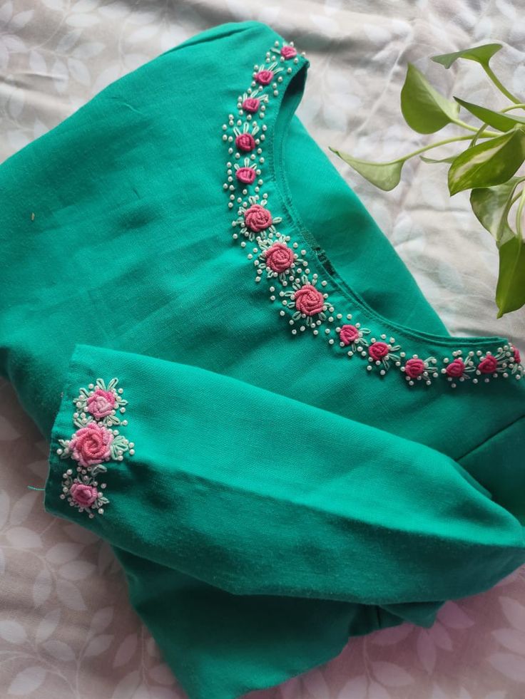 a green shirt with pink flowers on it and a plant in the corner next to it