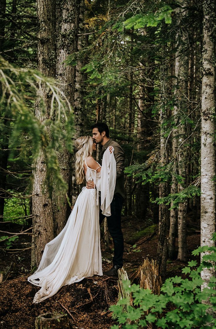 a bride and groom kissing in the woods