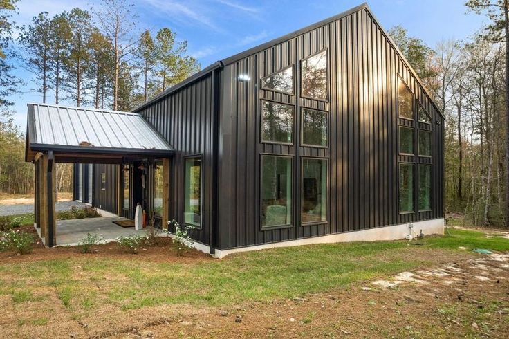 a black house with lots of windows on the front and side of it, surrounded by trees