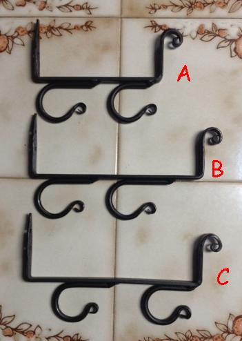 three black wrought iron hooks on a white tile wall with the letters a, b and c