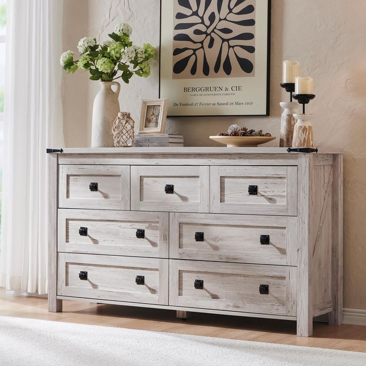 a white dresser with drawers and pictures on the wall