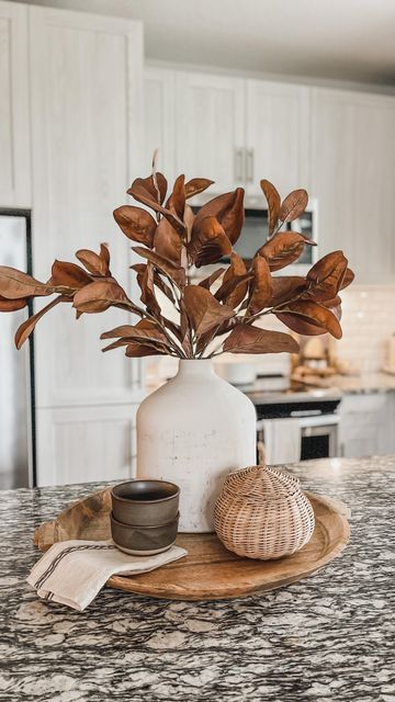 a white vase filled with leaves sitting on top of a wooden tray next to a bowl