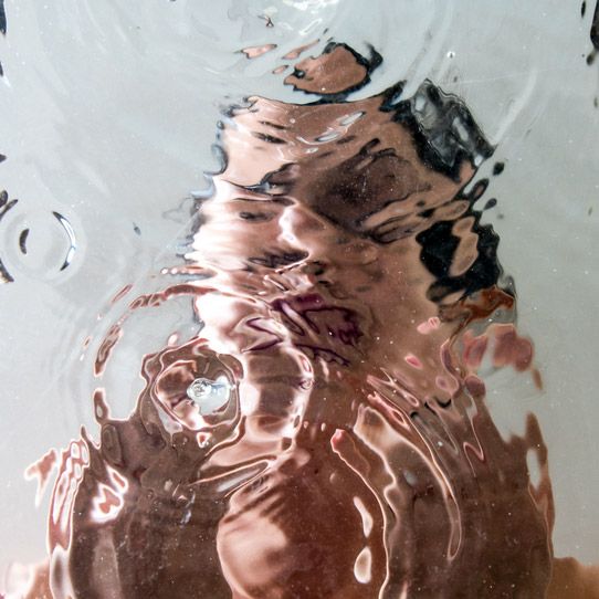 a person's reflection in the water with their hand under them and his face obscured by the water