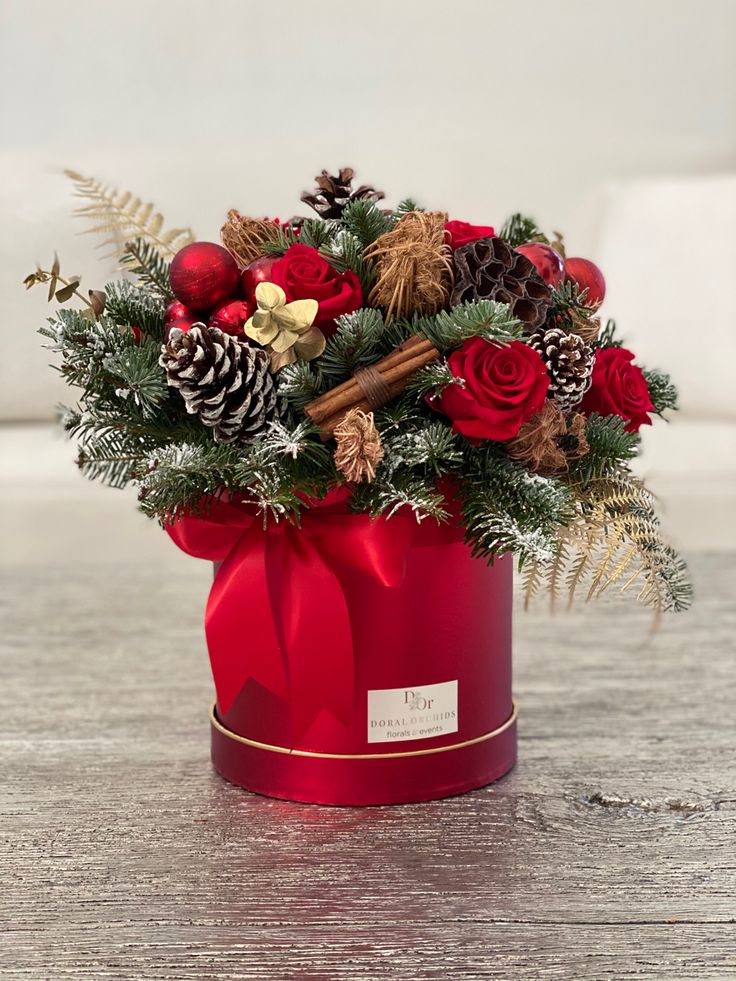 a christmas arrangement in a red box with pine cones, berries and other holiday decorations