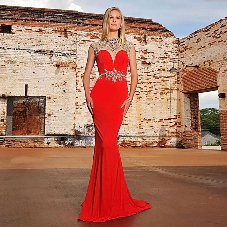 a woman in a long red dress posing for a photo with an old brick building behind her