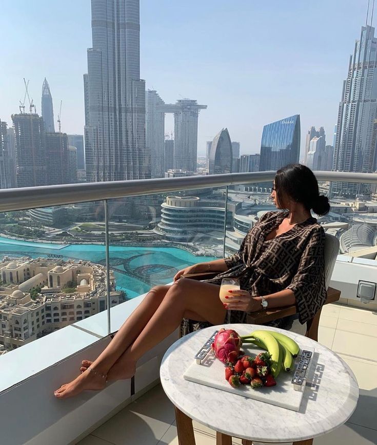 a woman sitting on top of a balcony next to a table filled with fruit and drinks