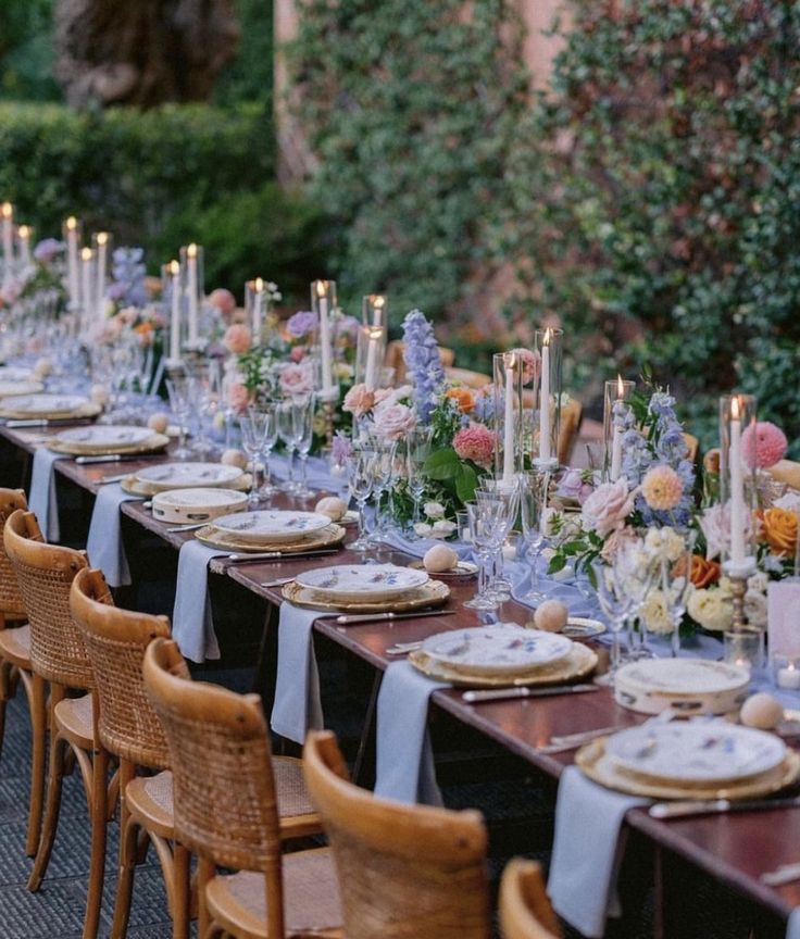 a long table is set with place settings and candles for an outdoor dinner party in the garden