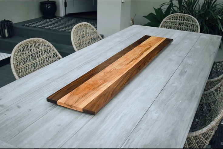 a long wooden plate sitting on top of a table next to wicker chairs and potted plants