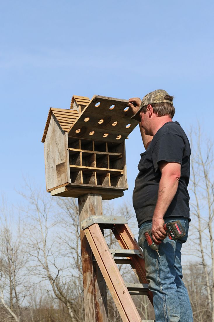 a man standing next to a wooden bird house