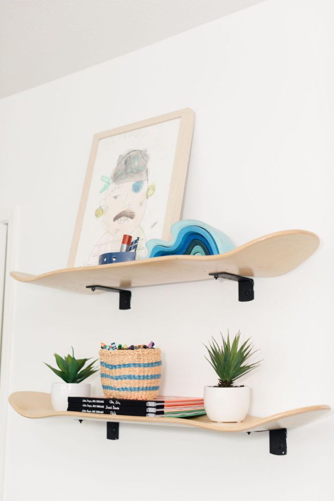 two wooden shelves with plants and books on them in the corner of a white room