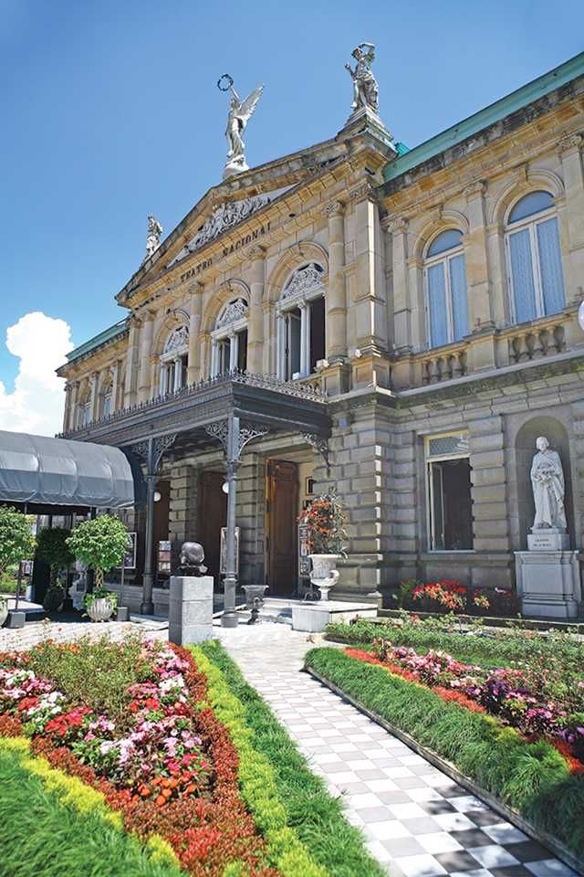 a large building with lots of flowers and statues in front of it on a sunny day