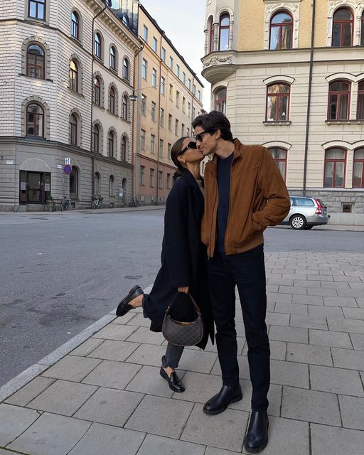 a man and woman standing on the sidewalk in front of some buildings