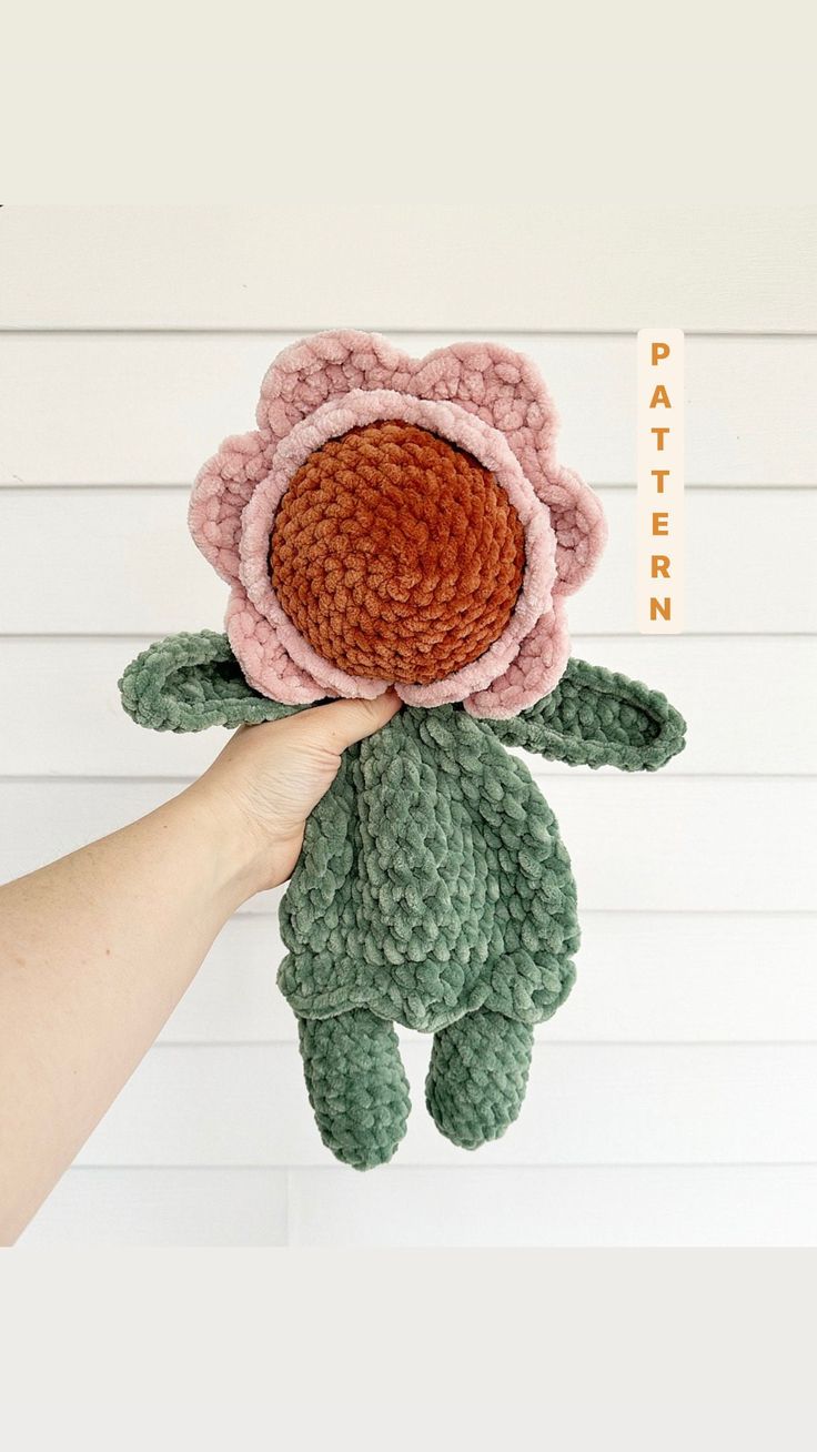 a hand holding a crocheted flower in front of a white wall with the words pattern on it