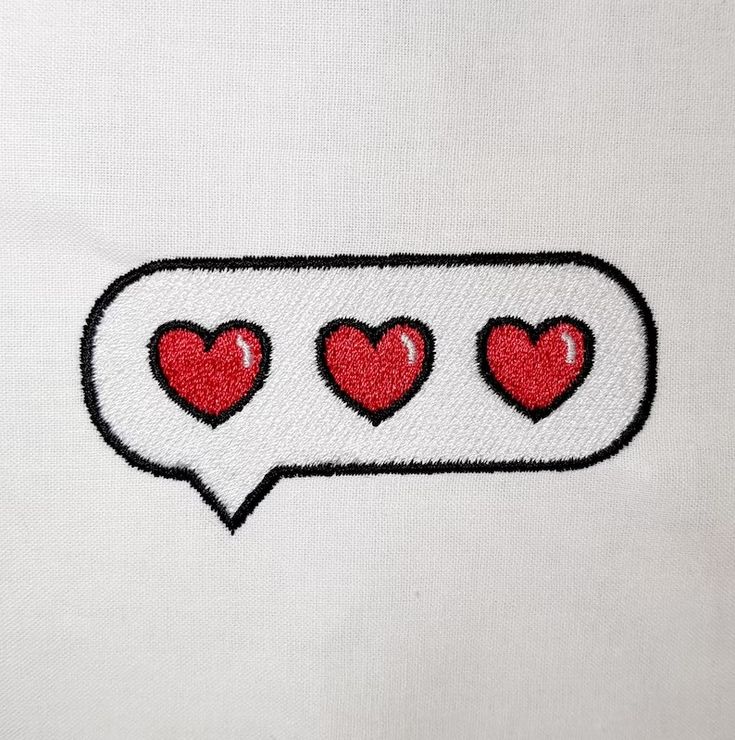 three red hearts in a speech bubble embroidered onto a white t - shirt with black trim