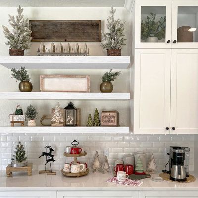 a kitchen with white cabinets and shelves filled with christmas decorations on top of it,