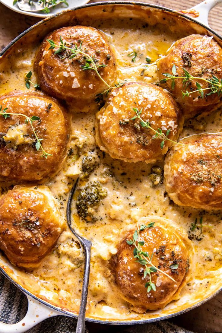 a skillet filled with baked potatoes covered in cheese and herbs next to a spoon