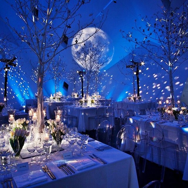 a room filled with lots of tables covered in white linens and decorated with trees