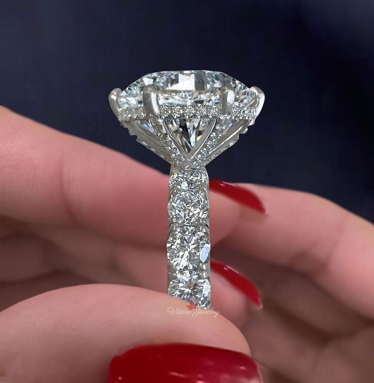 a close up of a person holding a diamond ring in their hand with red nails